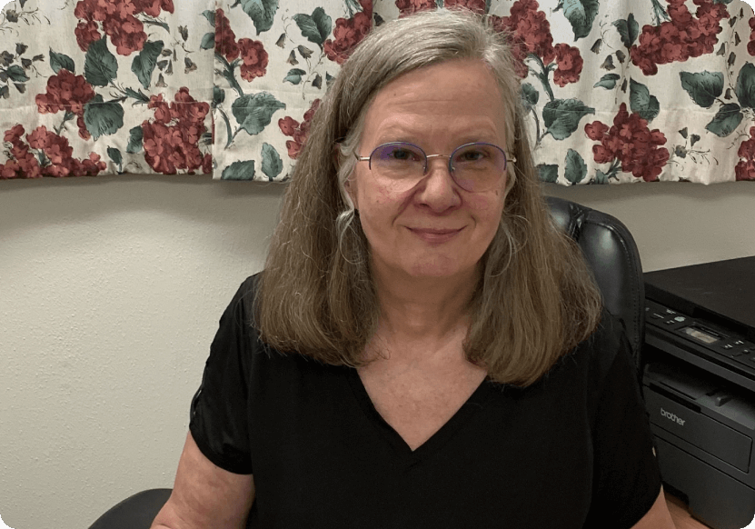 A woman with long hair and glasses sitting in a chair.