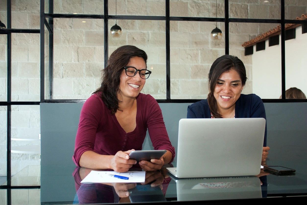 Two women sitting at a table looking at a laptop.